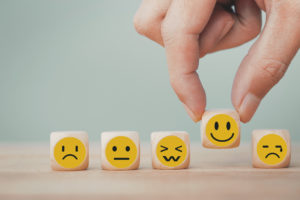 emotion faces on small cubes with a hand choosing the happy face